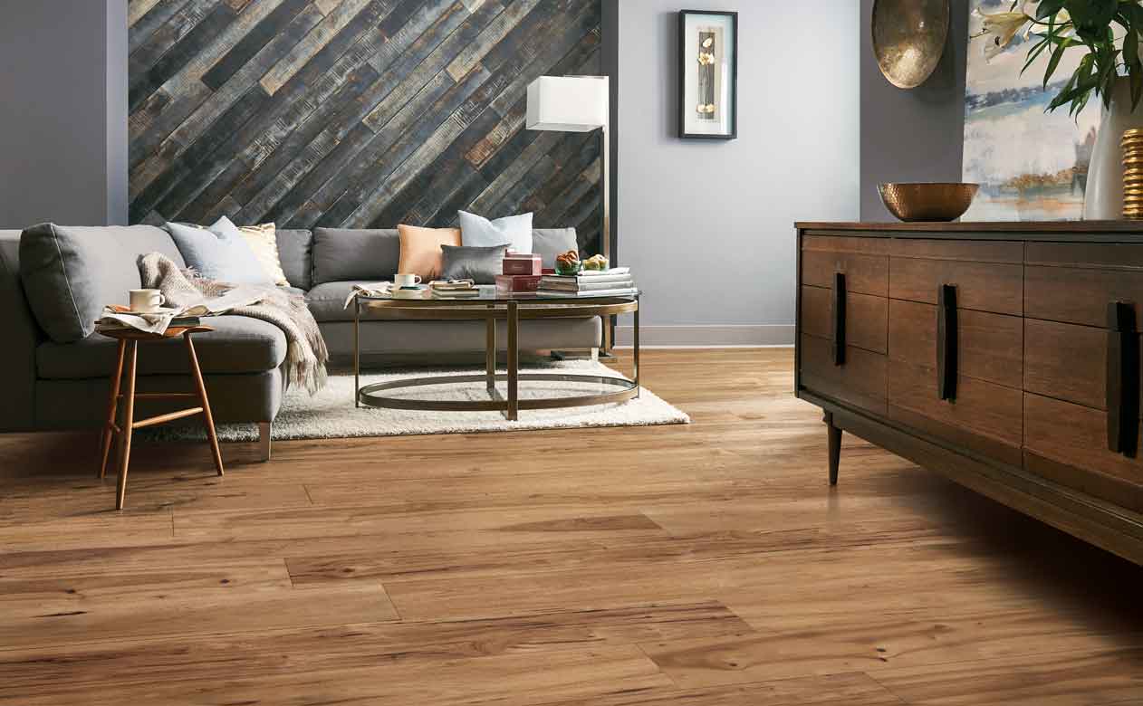 hardwood flooring in living area with large gray sectional and hardwood paneling on accent wall